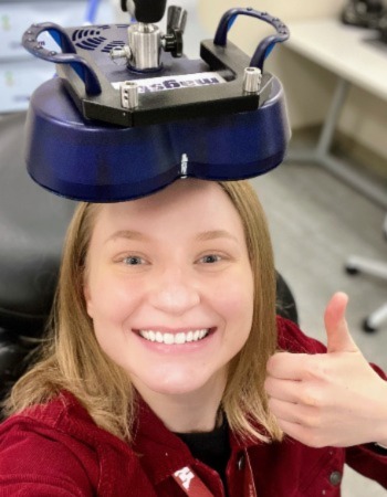 Alana smiling and giving a thumbs up with a TMS coil on her head.