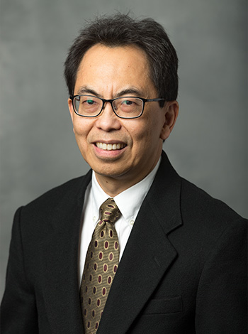 Dr Kelvin Lim smiling with a dark gray background